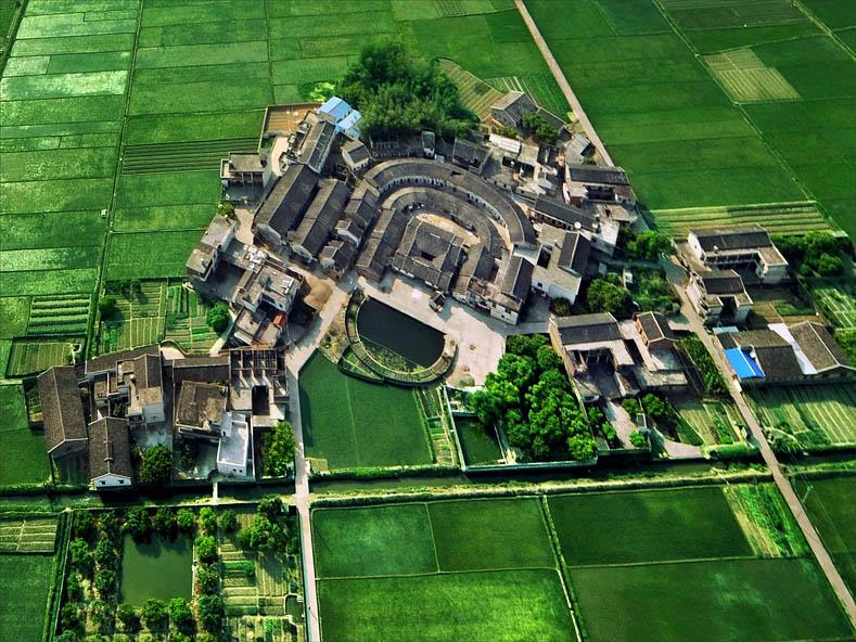 广州增城福和坳头岗埔村围垄屋实景图。图片展示了岗埔村典型的客家围垄屋，其圆形或半圆形的独特建筑结构和与周围池塘、自然环境的融合，体现了客家文化的居住智慧。